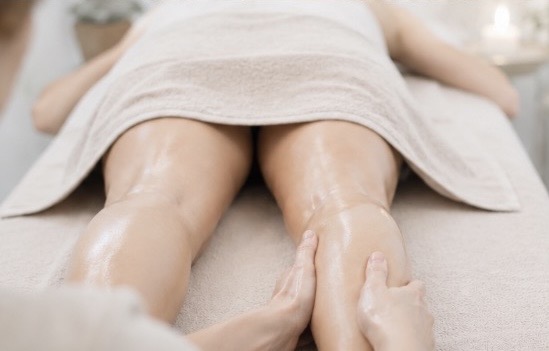 Massage ayurvédique - les racines de Virginie Jambes enduites d'huile avec des mais qui massent le mollet droit, avec une serviette beige posée sur les fesse de la femme qui se fait masser 